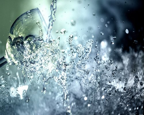 Close up shot of fresh clean water being poured into a clear glass on a wooden desk